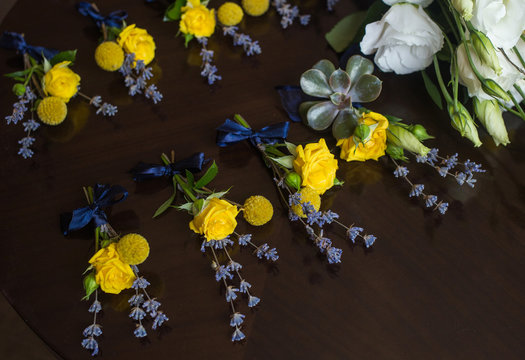 Closeup view of several small wedding floral boutonnieres made with yellow roses and violet flowers isolated on dark background. Horizontal color photography.