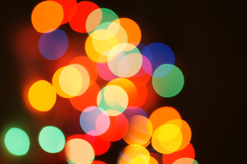 Multi-color holiday garland. Garland is blurred. Many colorful round lights. Fully defocused photo. Blurred background and foreground. Holiday mood. New Year and Christmas is coming.