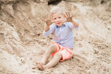 Portrait of cute happy white child showing his dirty sandy hands after playing with sand at river beach during summer weekend. Horizontal color photography.