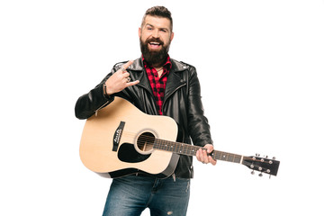handsome smiling musician in black leather jacket holding acoustic guitar and showing rock and roll sign, isolated on white