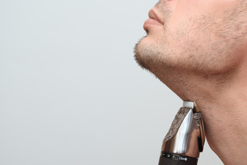 Cropped image side view of a young bearded man using electric shaver isolated over gray background....