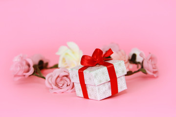 White gift box with a red bow on a pink background with flowers