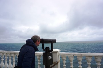 Obraz premium a man looks at the sea with his marine binoculars on the embankment in the city of Anapa.......