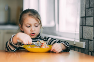 girl eating pasta with sausage in the kitchen in a striped jacket