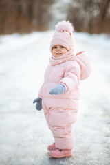 Little beautiful girl in pink jumpsuit in a snowy winter park