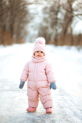 Little beautiful girl in pink jumpsuit in a snowy winter park