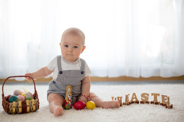 Fototapeta premium Cute little toddler child in sunny living room playing with Easter chocolate bunny and colorful Easter eggs
