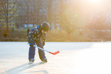 Naklejka premium Children, playing hockey and skating in the park on frozen lake, wintertime on sunset
