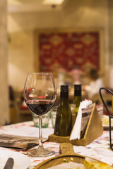 A glass of red wine on a table in a restaurant where a group of friends or family dine