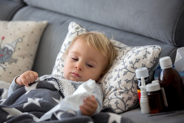 Sick child, toddler boy lying in bed with a fever, resting at home