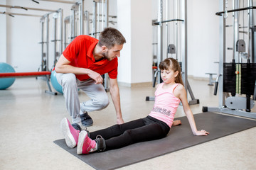 Trainer talking with young girl during the active treatment at the rehabilitation gym