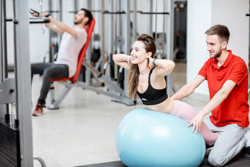 Young woman stretching on a fitness ball with man trainer during the spine treatment at the rehabilitation gym