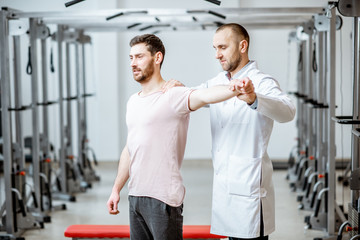 Fototapeta na wymiar Professional senior physiotherapist doing manual treatment to a man standing in the rehabilitation gym