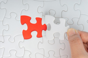 Fototapeta premium Hand put the last piece of jigsaw puzzle closeup to complete the mission. Selective focus and crop fragment