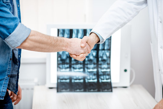 Handshake of the doctor and patient on the tomography print background at the therapist office