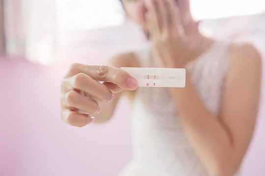 Pregnant asia woman in white dress hole and show a pregnancy test strip with happy and excited, close up of pregnancy test strip