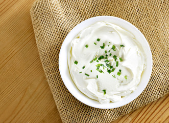 Cream cheese, quark or yogurt in a white bowl. Dairy product with fresh herbs, healthy eating theme. wooden table background.