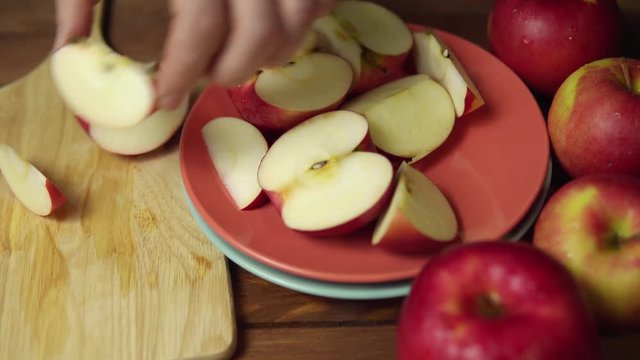 Closeup of a man cuts a red apple into halves and quarters with a knife. Ripe juicy fruit cut into pieces on a chopping wooden board,dolly shot.