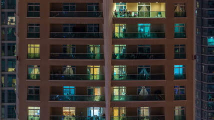 Fototapeta na wymiar Glowing windows in multistory modern glass residential building light up at night timelapse.