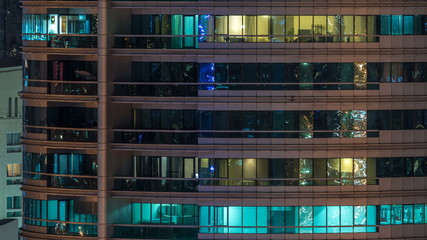 Fototapeta na wymiar Glowing windows in multistory modern glass residential building light up at night timelapse.