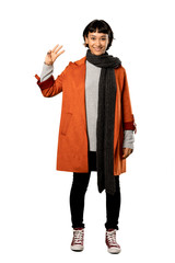 A full-length shot of a Short hair woman with coat happy and counting three with fingers over isolated white background