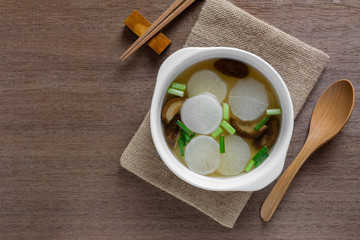 top view of white radish clear soup in a ceramic bowl on wooden table. asian homemade style food...