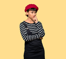 Young woman with beret having doubts and thinking over yellow background