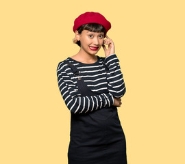 Young woman with beret having doubts while scratching head over yellow background