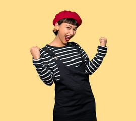 Young woman with beret celebrating a victory over yellow background