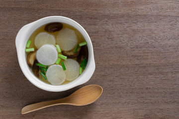 top view of white radish clear soup in a ceramic bowl on wooden table. asian homemade style food concept.