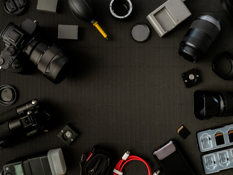 top view of work space photographer with digital camera, flash, cleaning kit, memory card, external harddisk, USB card reader, laptop and camera accessory on black table background.