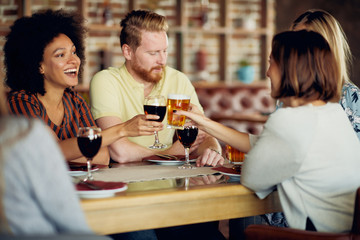 Friends making a toast while sitting in restaurant. Multi-ethnic group.