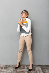 Full length photo of caucasian businesswoman wearing glasses holding paper folders in the office, isolated over gray background