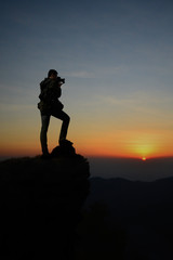 Dark silhouette of man photographer on the cliff and beauty sunrise in the morning.