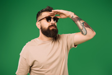 tattooed man in sunglasses looking away, isolated on green