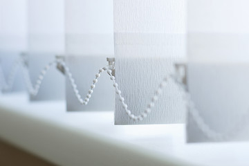 A row of white vertical blinds cover the sunlight from the window. Close up.