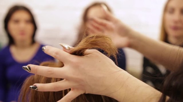 The girl does her hair on the head of a mannequin at a hairdresser's courses in the salon on a blurred background of watching students.Practical lesson in the school of hairdressers. Long hair styling