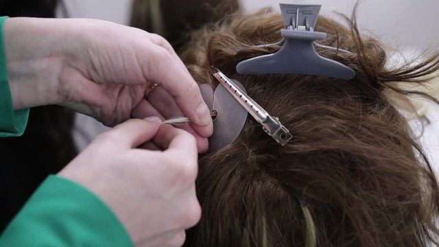 Hairdresser is engaged in artificial hair extensions in the beauty salon. The process of Capsule hair extension. Cold tape build-up