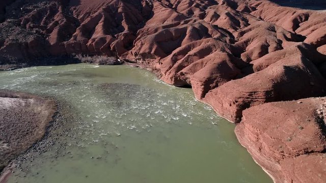 Aerial view looking down at small rapids in the Colorado River next to red rock desert terrain in Moab Utah.