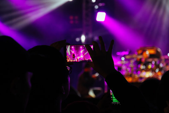 Hand hold a smart phone taking photo or recording video of concert stage