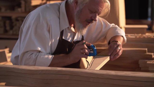 Portrait of Professional Old Joiner doing Measurements with Tools on Furniture Production. Skillful Carver Works with Professional Tools for Oak . He has Special Uniform. Handicrafts. Wood Carving.