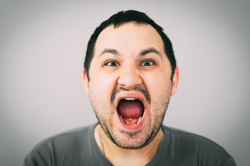 Portrait of young man screaming with beard in grey t-shirt