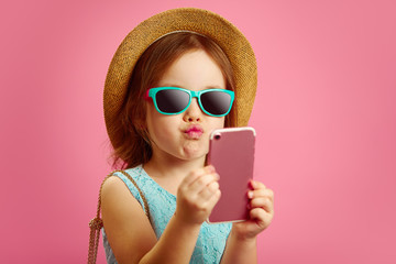 Funny little girl makes a selfie portrait on phone, pulls her lips to the camera, wears a straw hat...