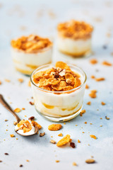 Healthy breakfast or dessert. Tasty corn flakes with yogurt, almond and honey in a small glass on light blue background. Copy space for text.