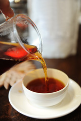 Pour freshly brewed black tea from a glass jug into a ceramic tea bowl