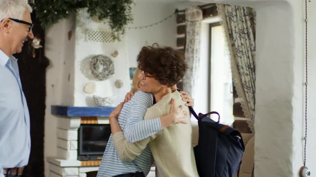 Medium shot of young woman with short curly hair entering home of her relatives and hugging them