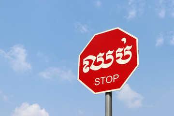 Stop sign on blue sky background in Cambodian language and English.