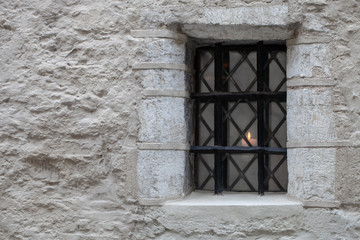 Barred window in an old stone house. The candle is burning in the window