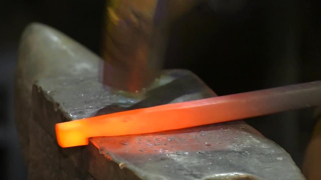 The smith behind work. In hands at the smith nippers which he holds the warmed piece of metal. Leaning on an anvil the smith forges a metal figured detail. Metal red from temperature