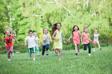 A group of happy children of boys and girls run in the Park on the grass on a Sunny summer day . The concept of ethnic friendship, peace, kindness, childhood.